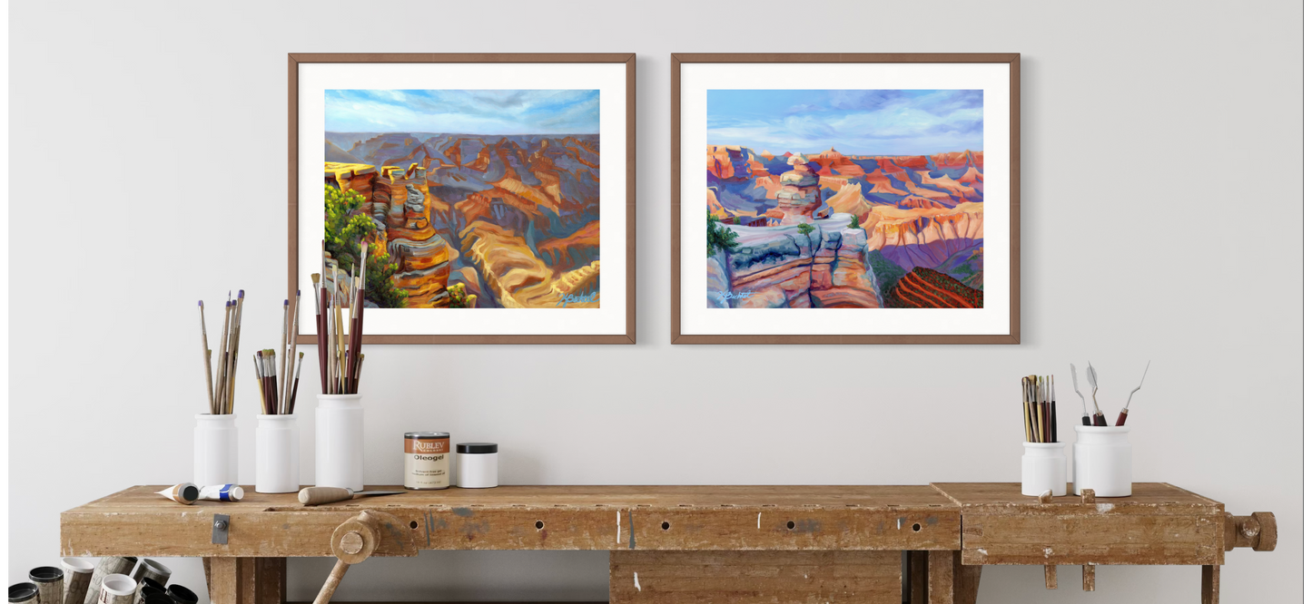 Two framed artworks of a landscape on a wall above a wooden desk with decorative items.