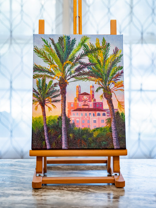 Painting of palm trees and a building on an easel with a blurred background