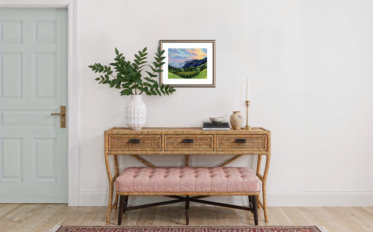 Entryway with a wooden console table, pink bench, and framed landscape art on a white wall.
