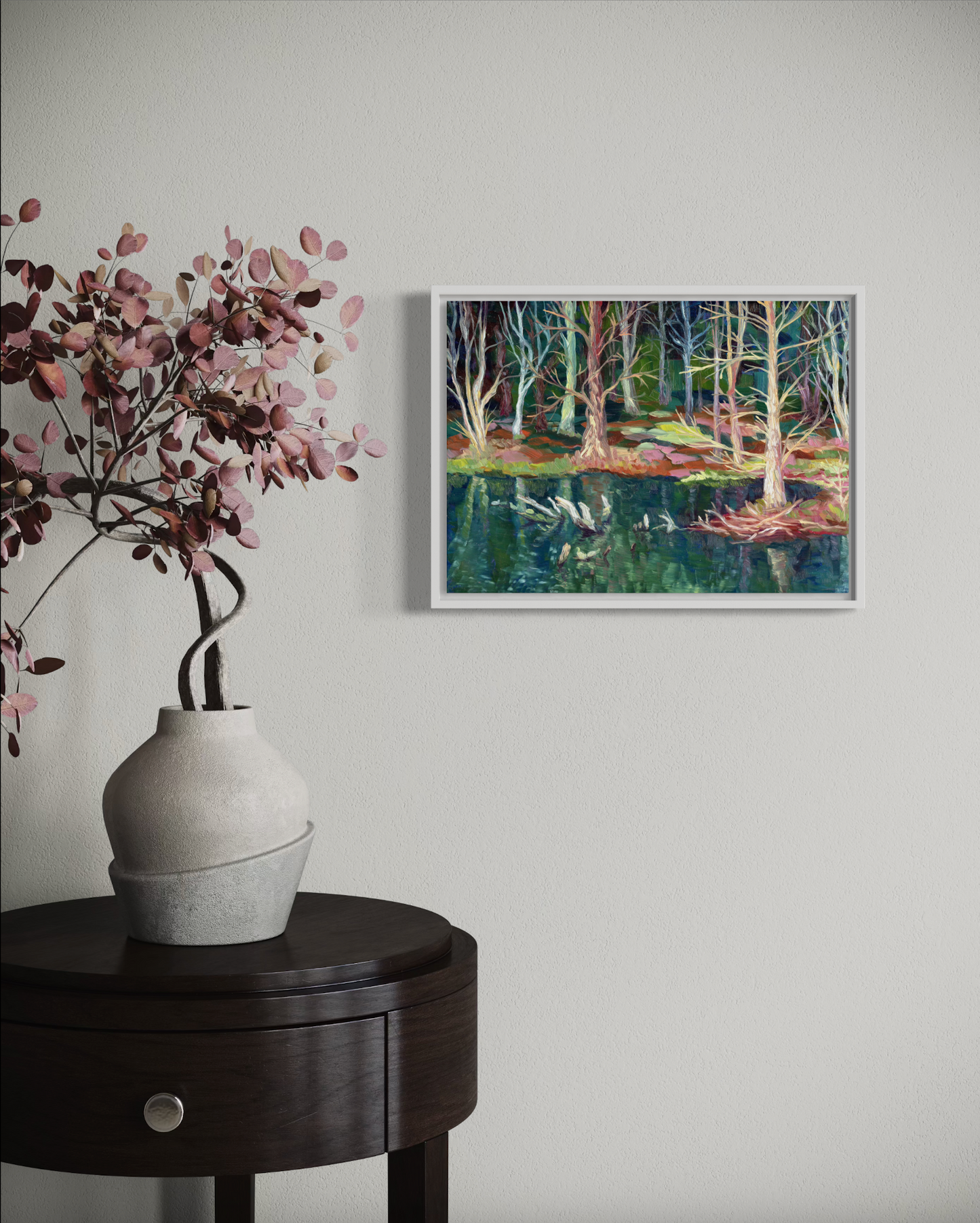 Framed artwork of a forest scene on a wall above a vase with flowers on a table.