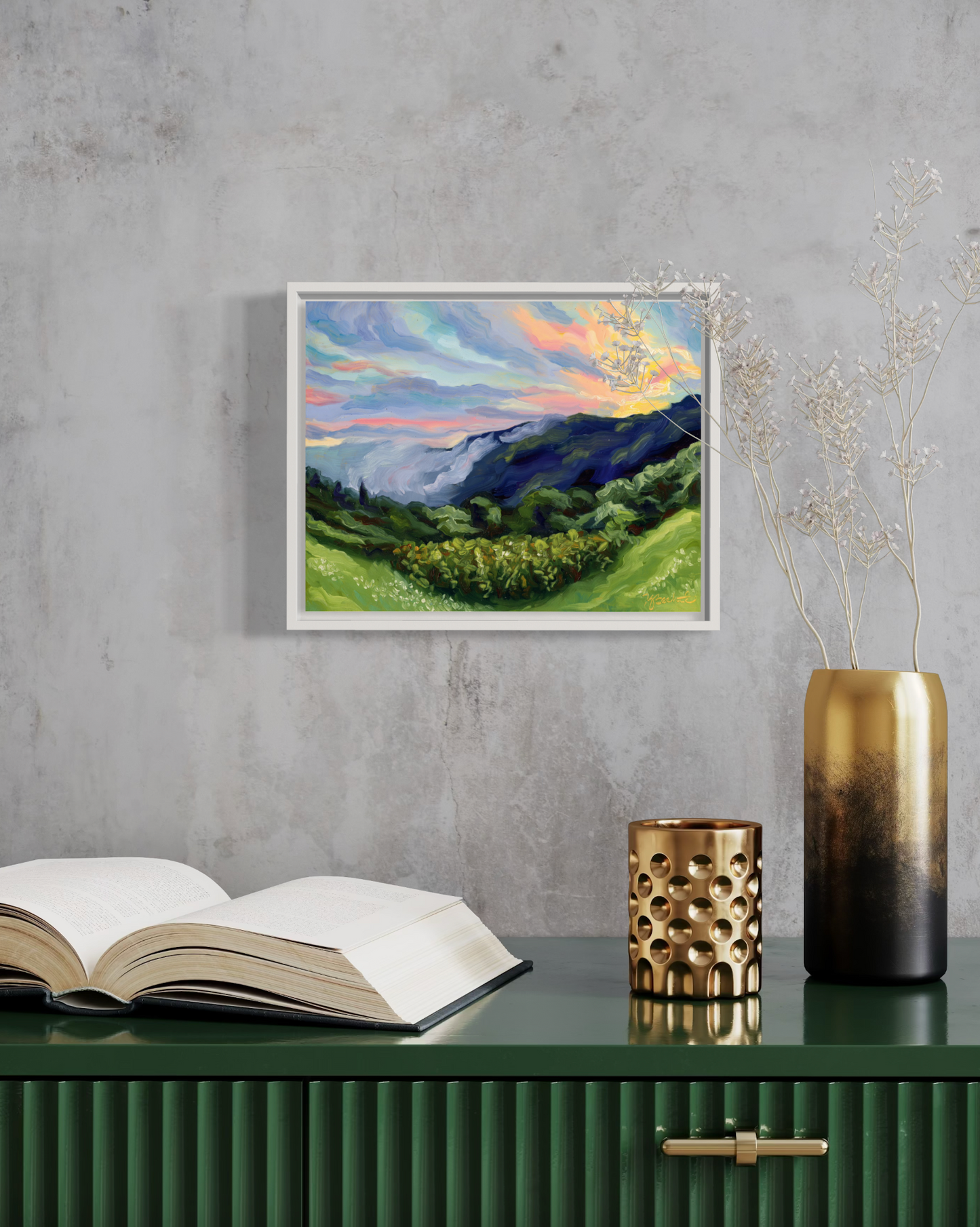 Framed landscape painting on a wall above a table with an open book and decorative items.