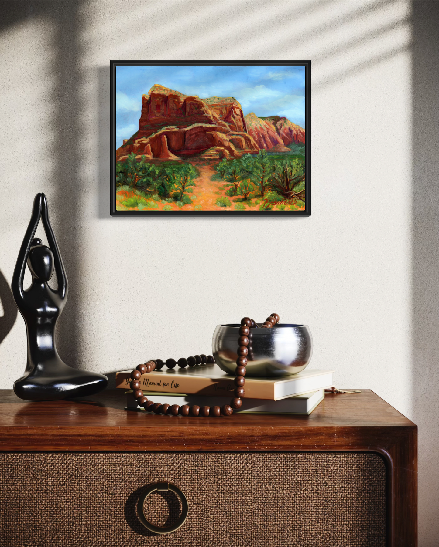 Framed artwork of a desert landscape on a wall above a wooden console table with decorative items.