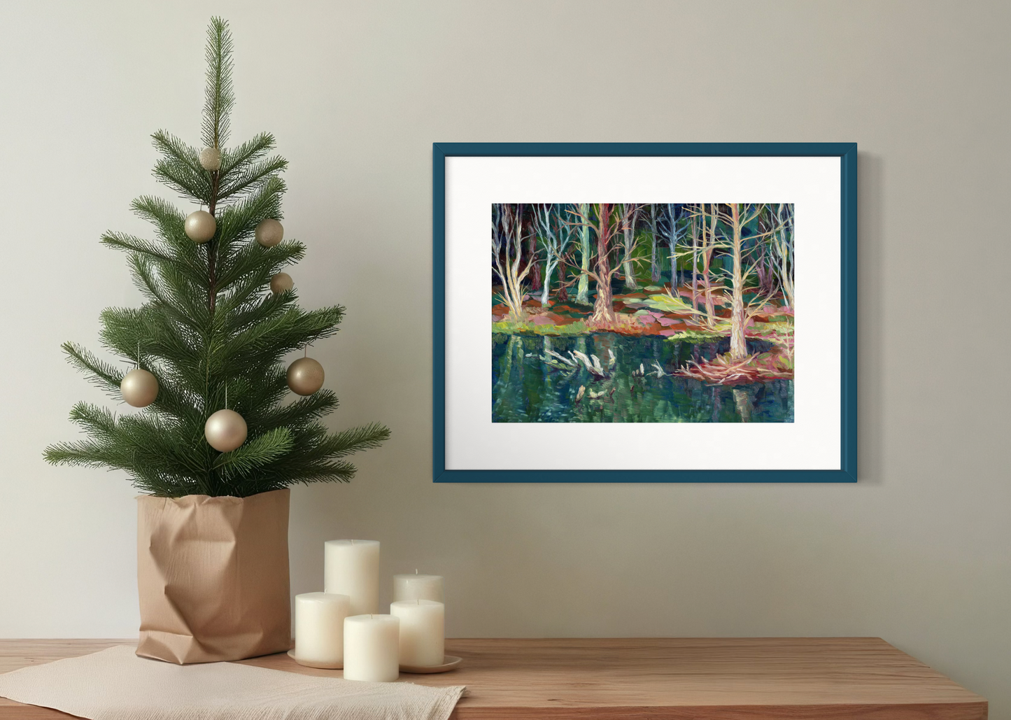 Framed artwork of a forest scene on a wall above a Christmas tree and candles.
