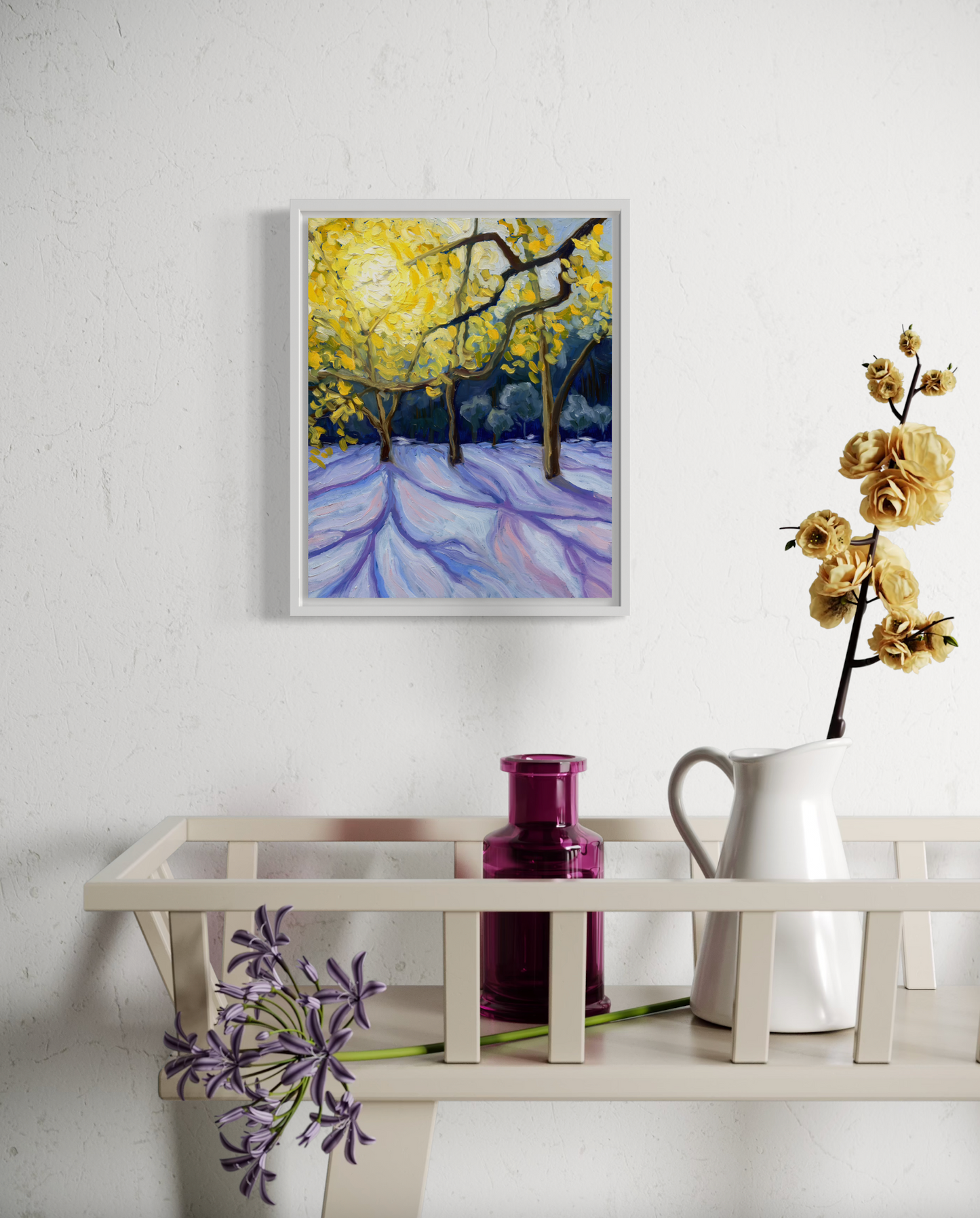 Framed painting of a snowy landscape with trees on a white wall above a shelf with decorative items.