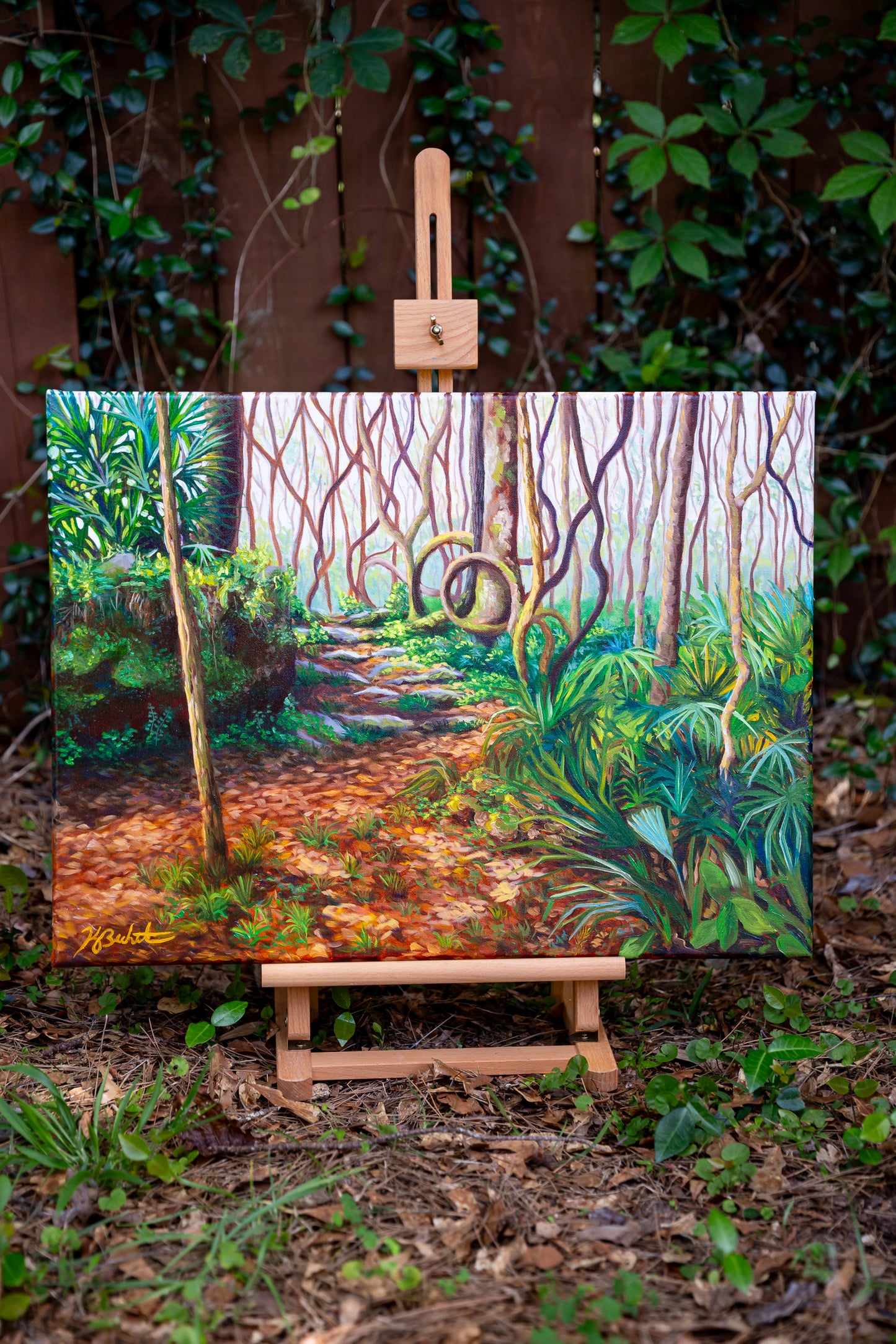 Painting of a forest scene on an easel surrounded by greenery