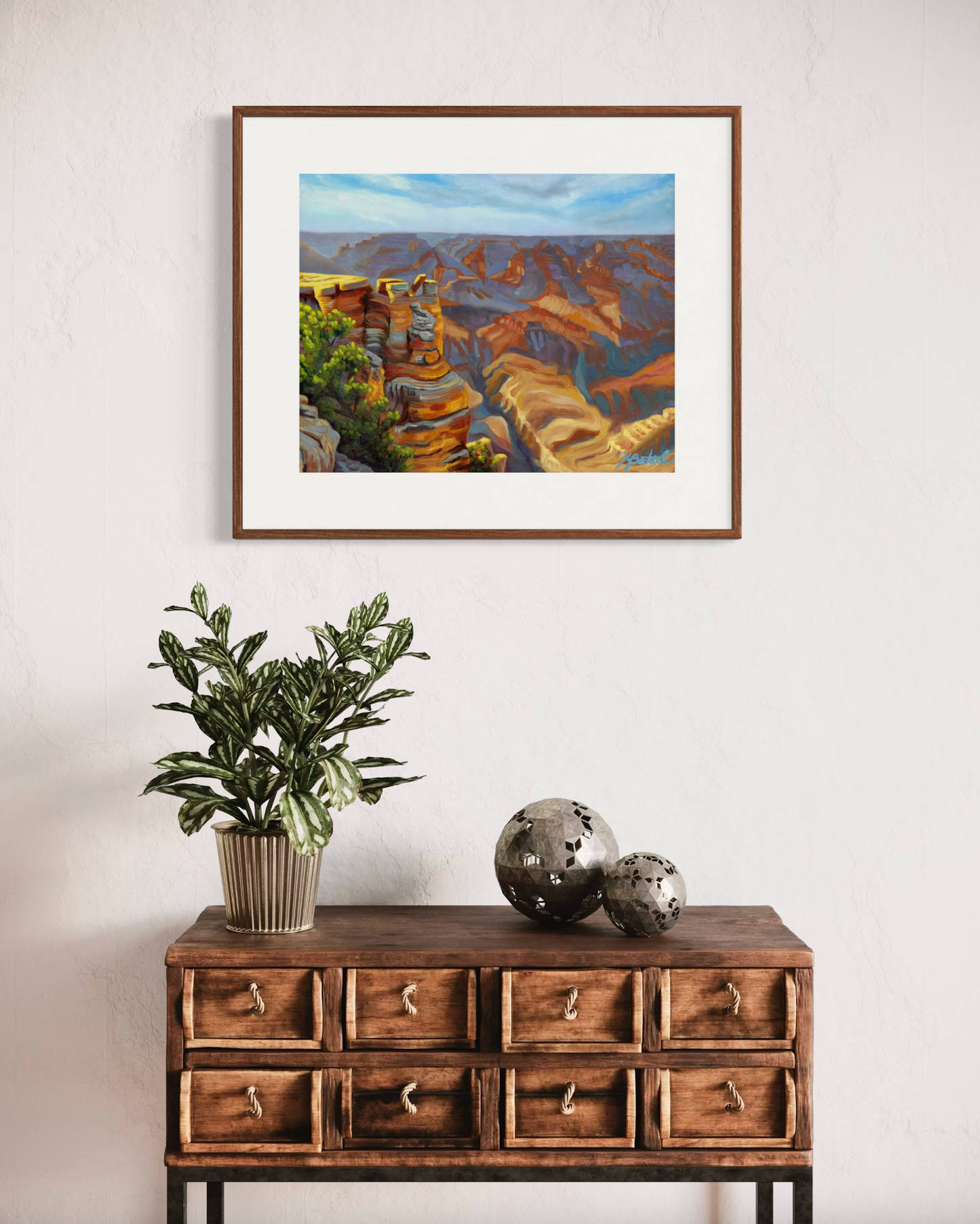 Framed landscape painting above a wooden console table with decorative items.