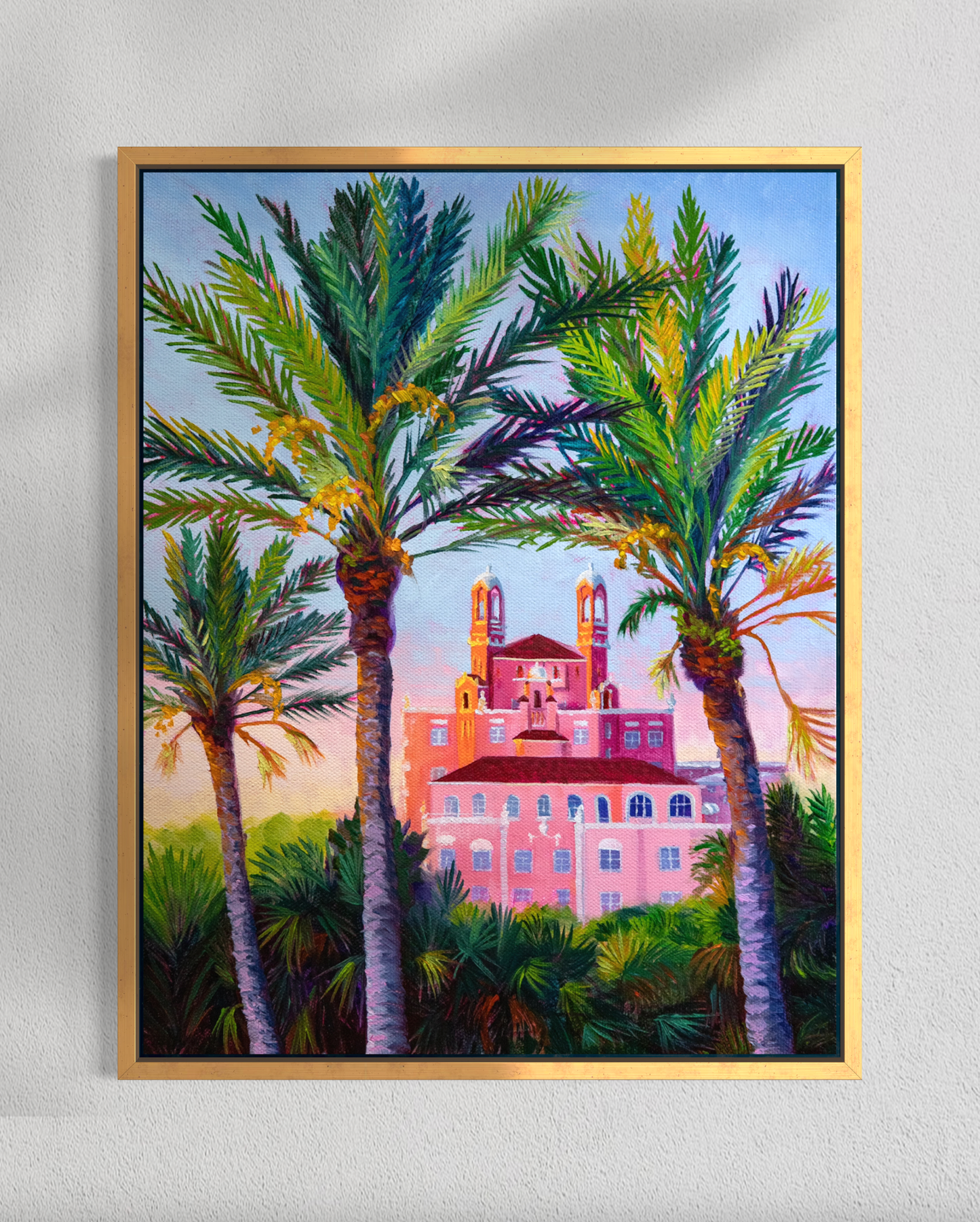 Framed artwork of a pink building with palm trees on a white wall