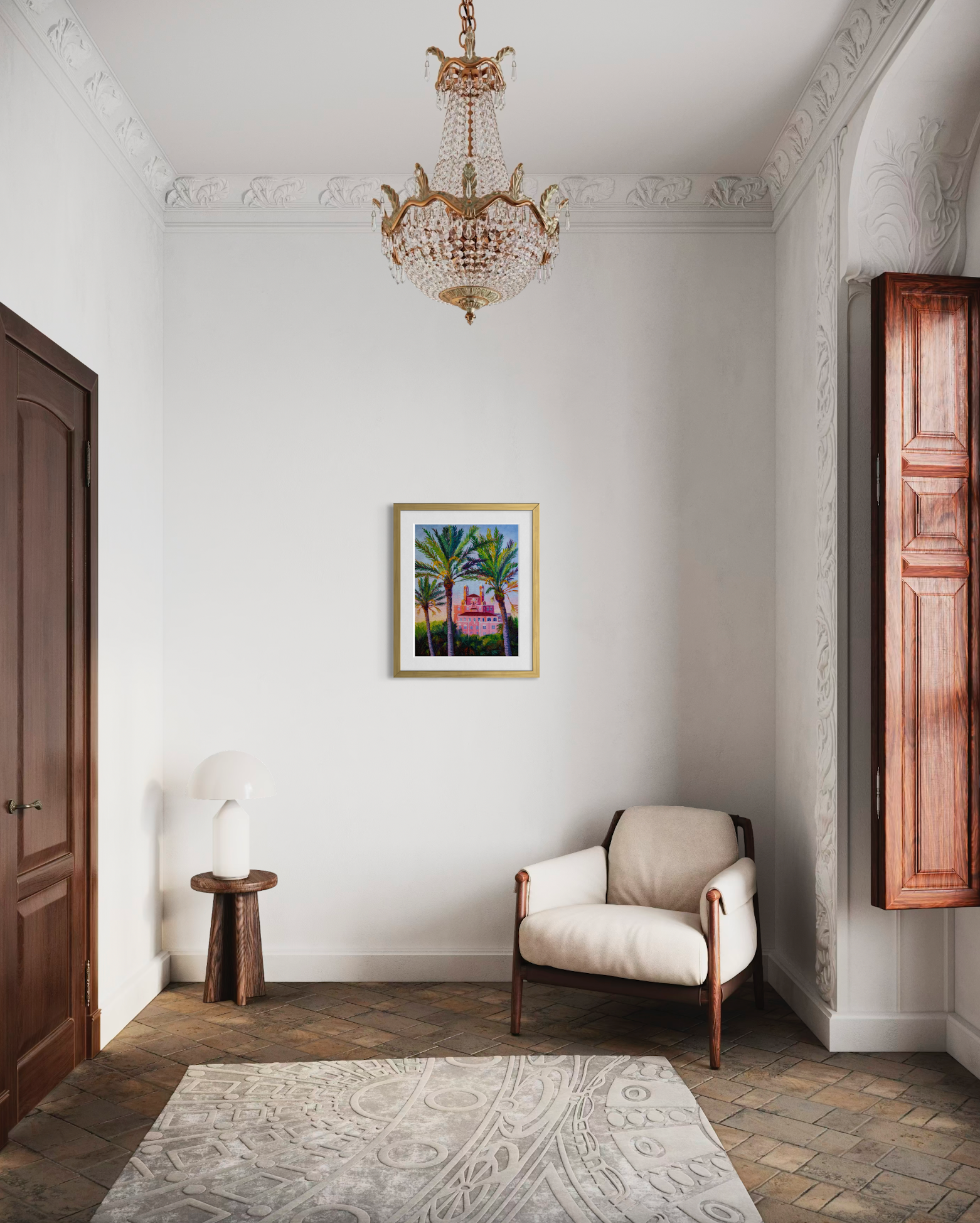 Elegant interior with a chandelier, armchair, and framed artwork on a white wall. Artwork is a framed print of palm trees and an ornate pink building.