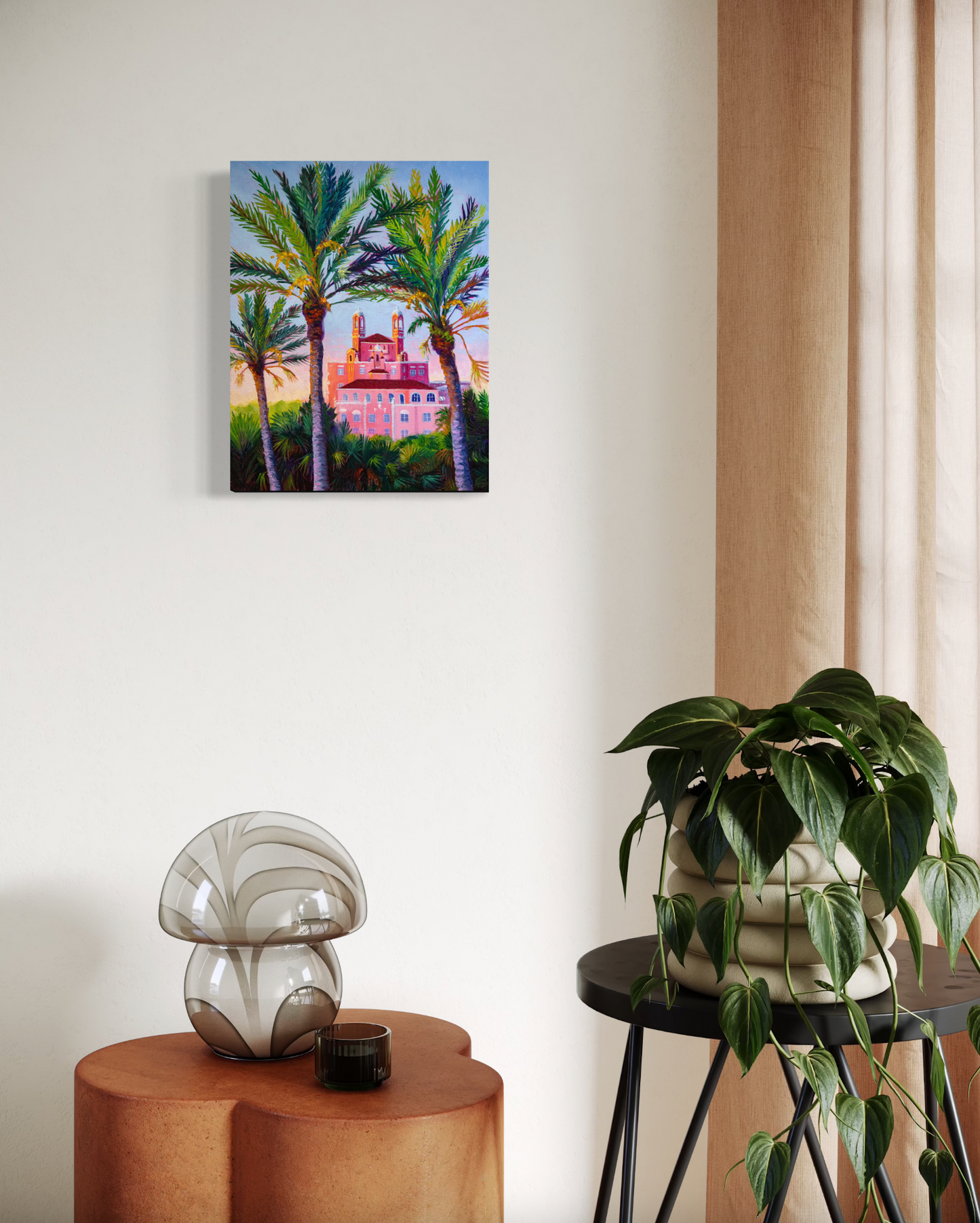 Painting of a tropical scene with palm trees and a building, hanging on a wall above a side table with decorative items.