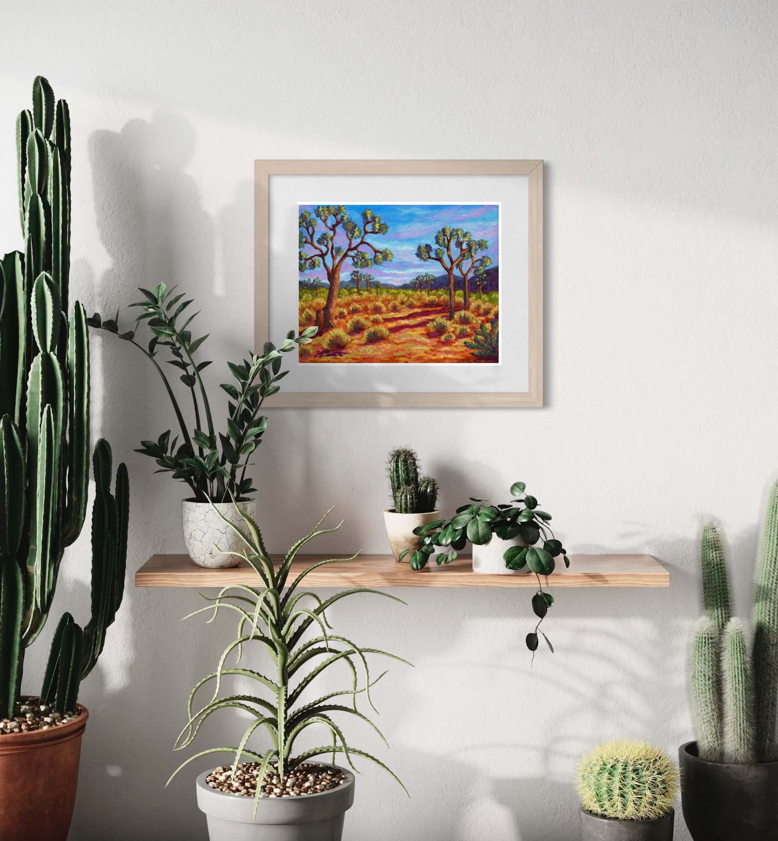 Framed artwork of a desert landscape on a wall with potted plants below.