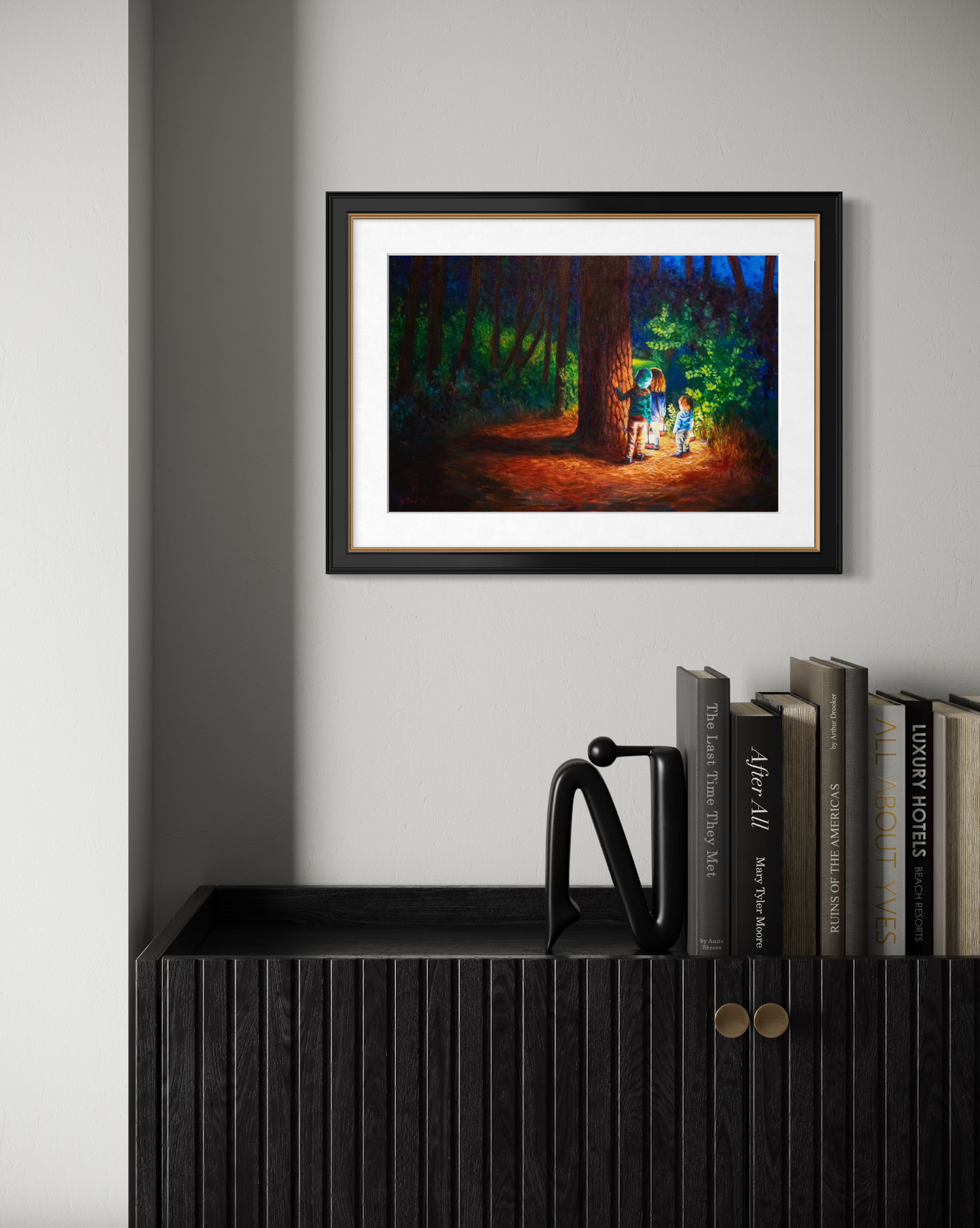 Framed artwork of a forest scene with two figures on a wall above a shelf with books.