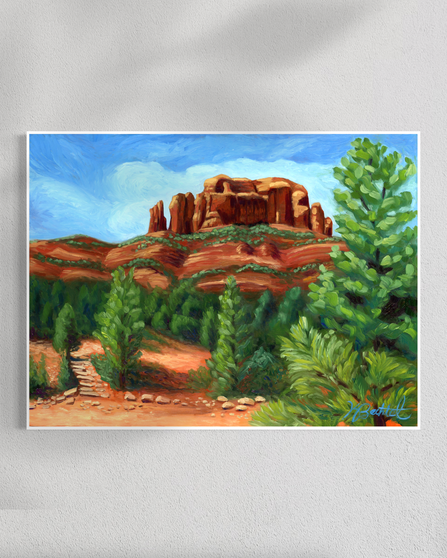 Painting of a desert landscape with red rock formations and green trees on a white wall.