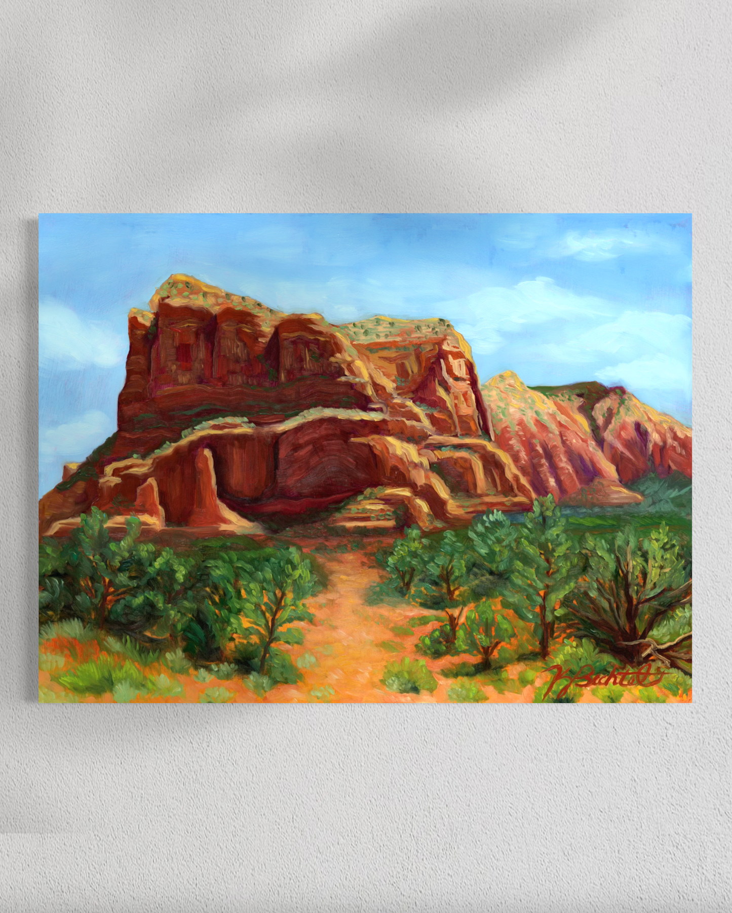 Painting of a desert landscape with red rock formations and green shrubs.