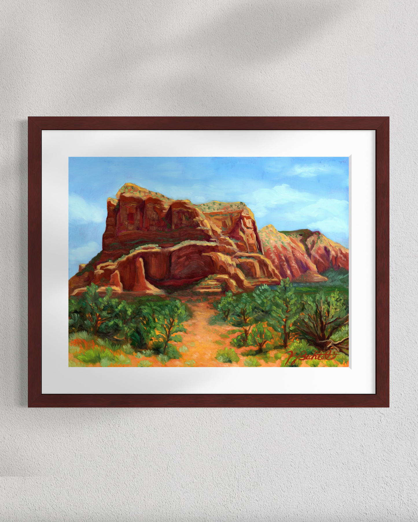 Framed painting of a desert landscape with red rock formations and greenery.
