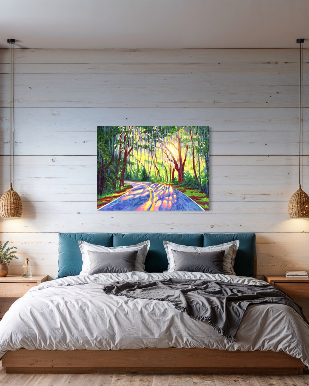 A colorful canvas painting of a sunlit forest road with trees and a yellow-orange center line, displayed on a white wood-paneled wall above a bed in a styled bedroom.