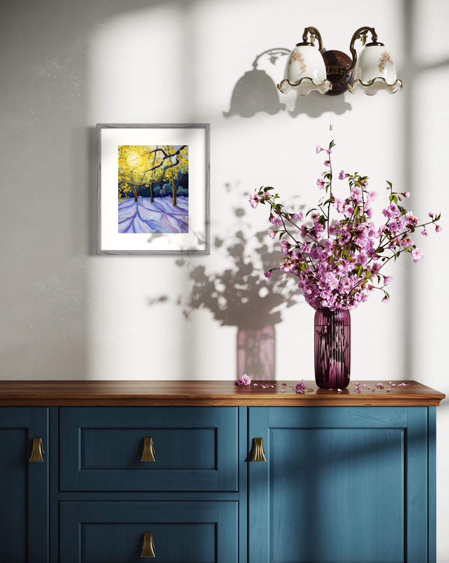 Blue cabinet with a wooden top, pink vase with flowers, and framed artwork on a white wall.