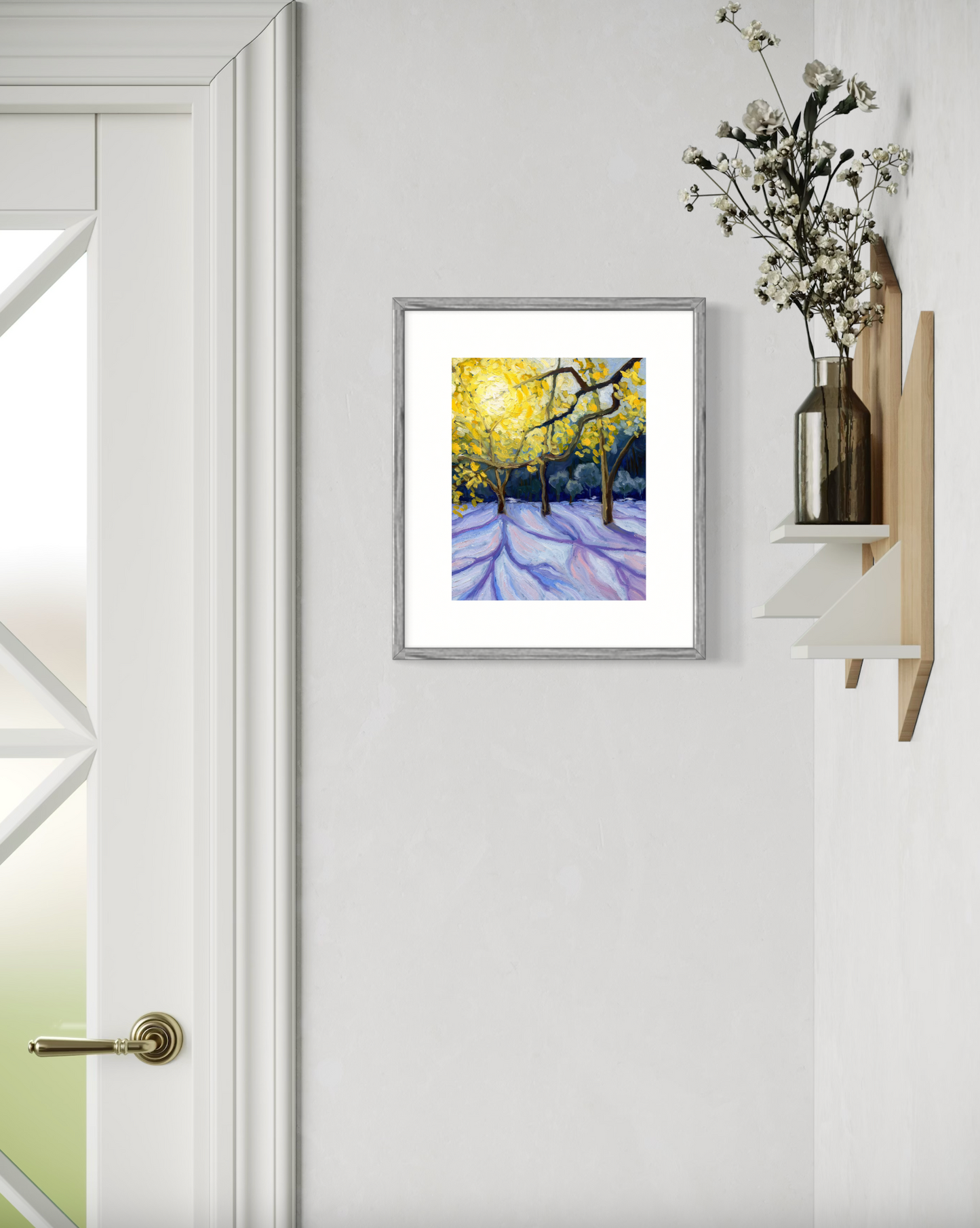 Framed artwork of a snowy landscape with trees on a white wall next to a door.