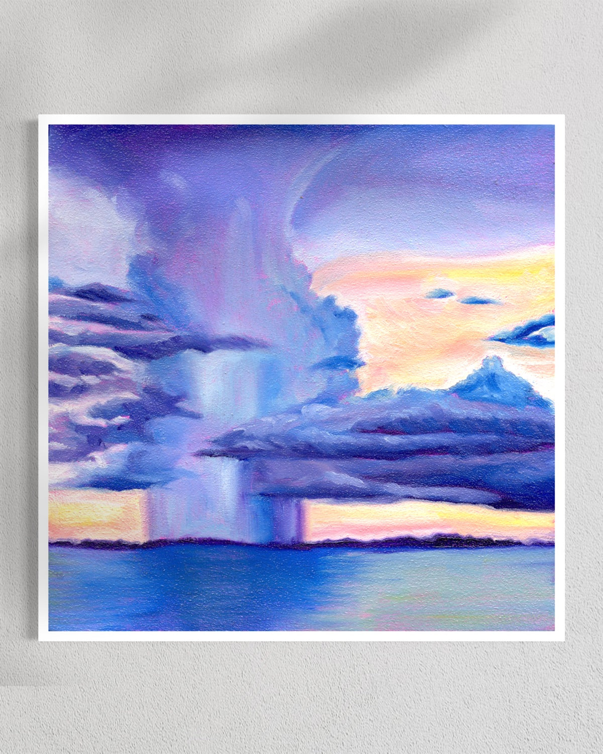 A square art print depicting a dramatic storm scene with a large purple and blue cloud formation over water, under a pastel sky with pink, yellow, and blue tones, shown against a light gray wall.