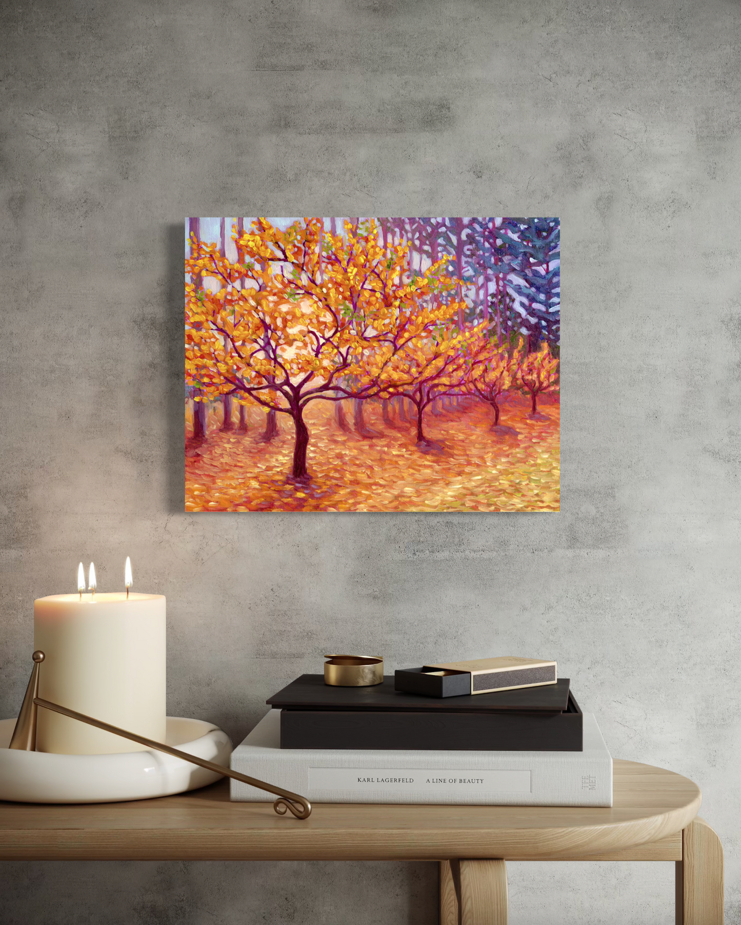 Mockup of Canvas print of artwork showing trees with autumn colors on a gray wall above a table with books and a candle.