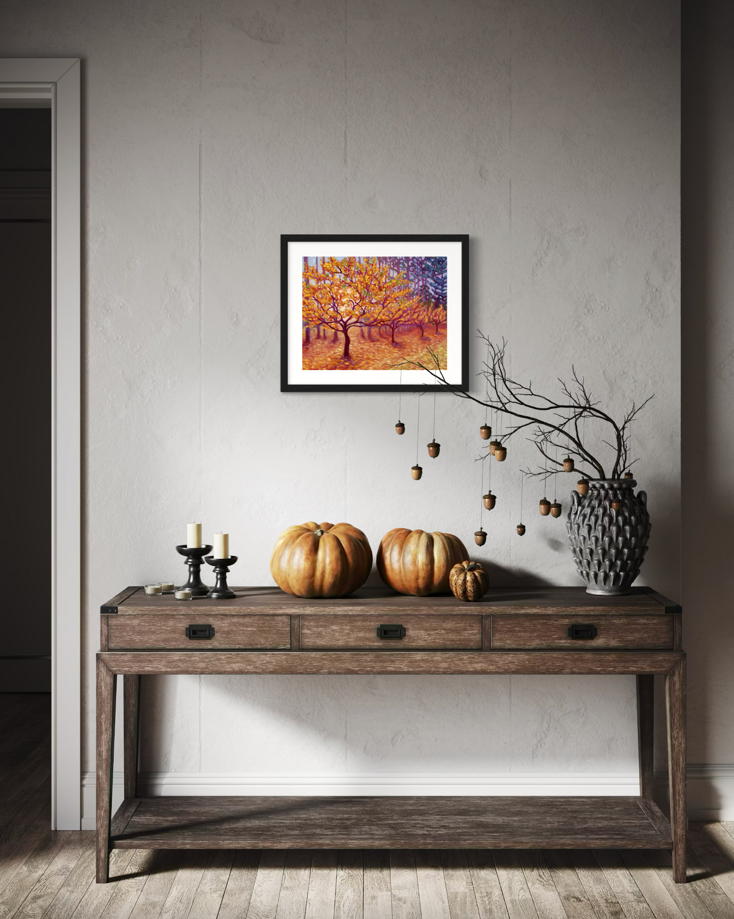 Decorative console table with pumpkins and a framed artwork of golden trees on a wall.
