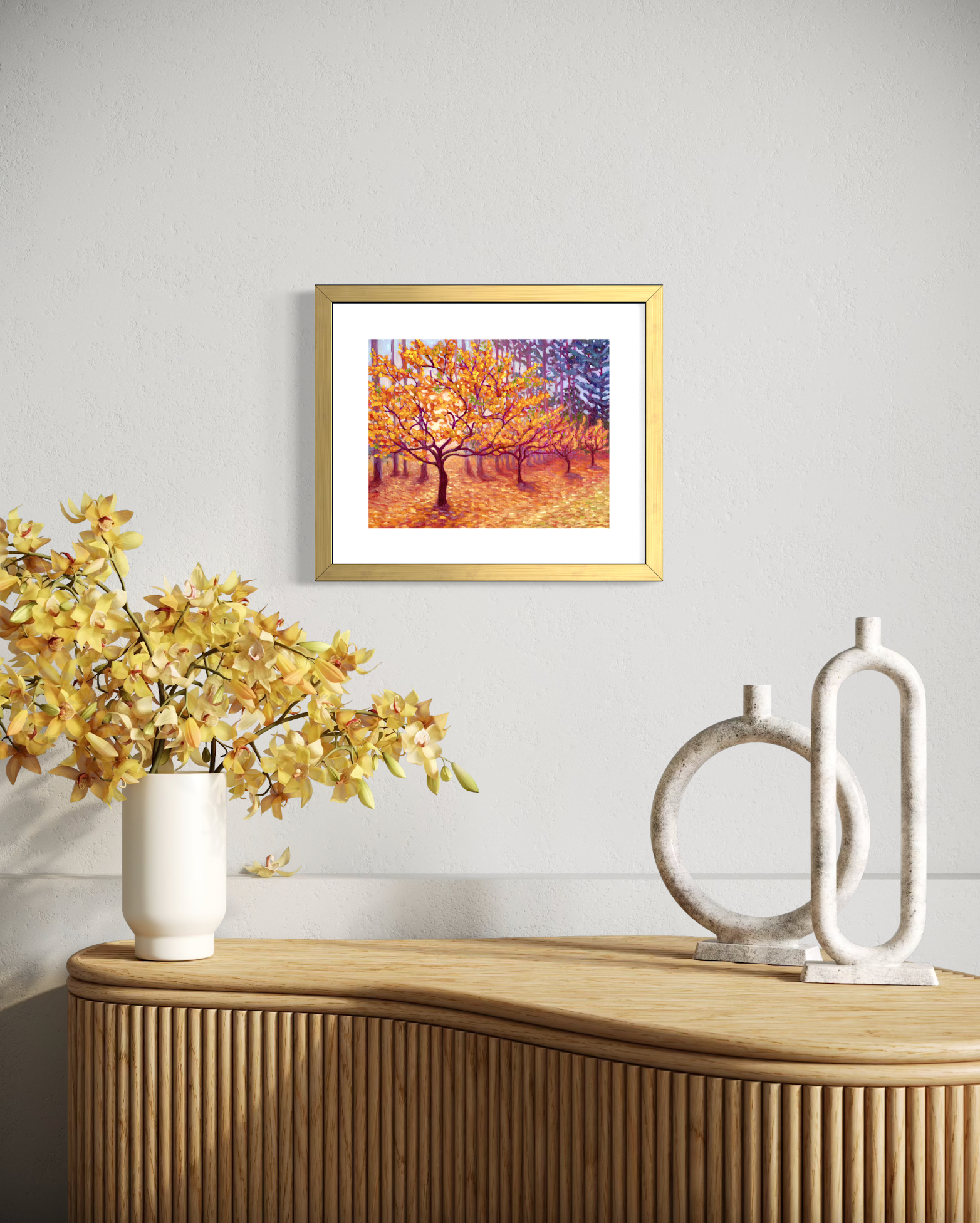 Framed artwork in a gold frame with white matte of a tree with autumn leaves on a wall above a wooden console table with decorative items.