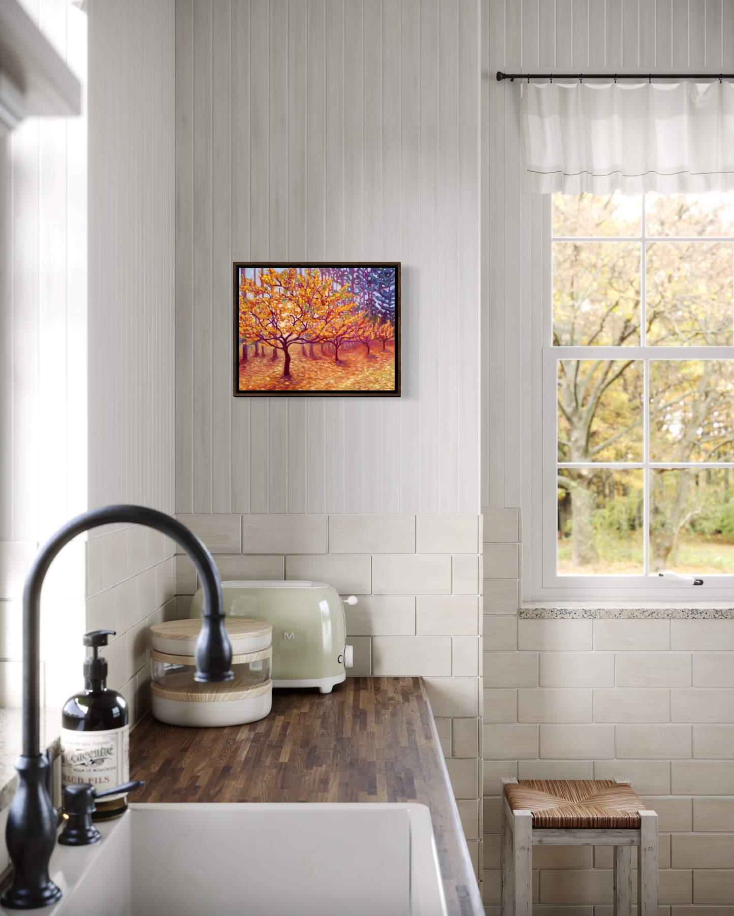 Kitchen interior with a sink, window, and wall art of a row of golden trees.