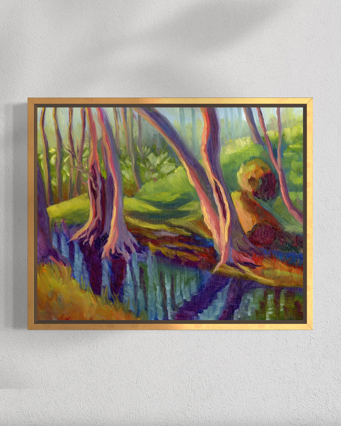 Framed painting of a forest scene with trees and a stream on a white wall.