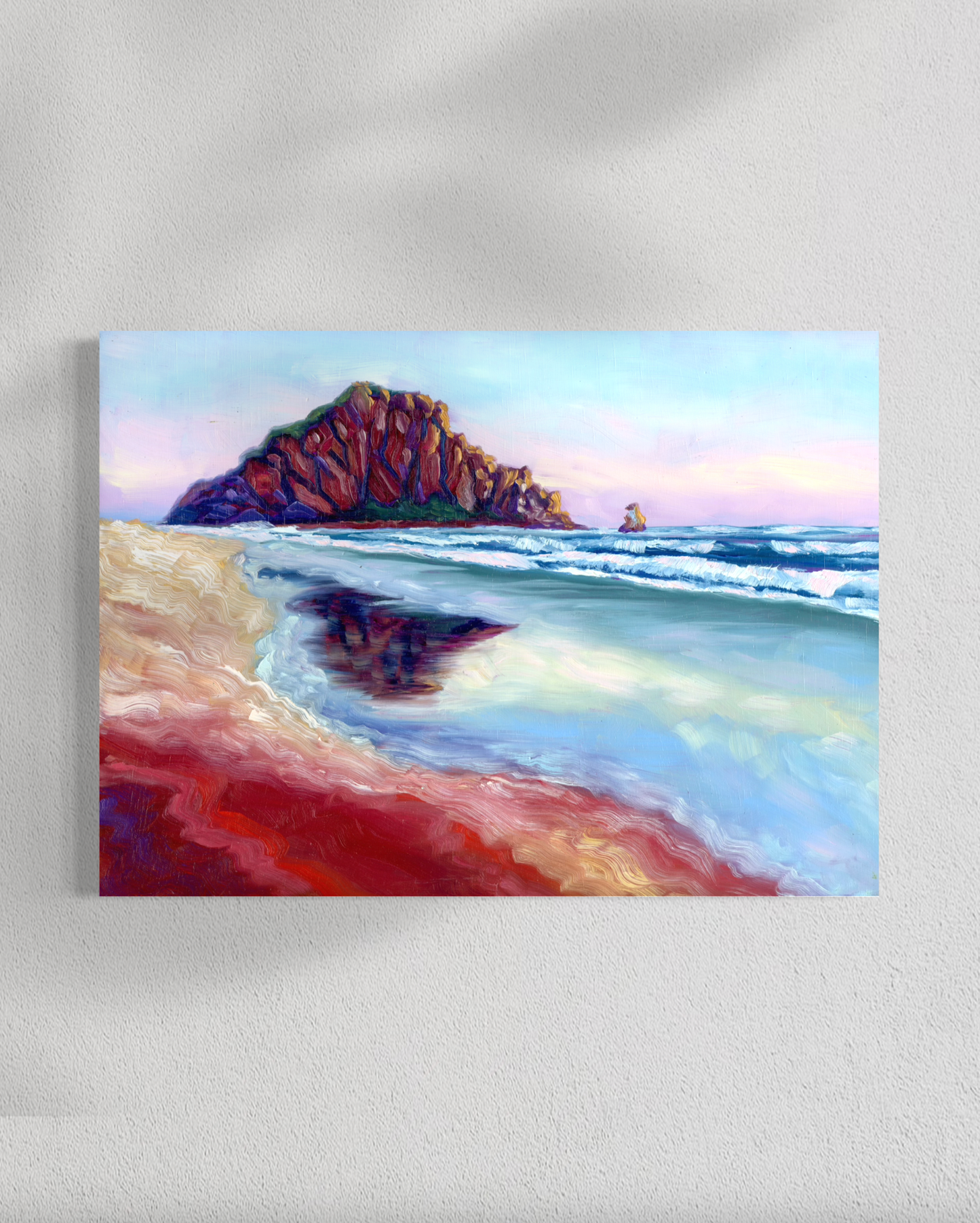 Painting of a beach scene with a large rock formation and ocean waves on a white wall.