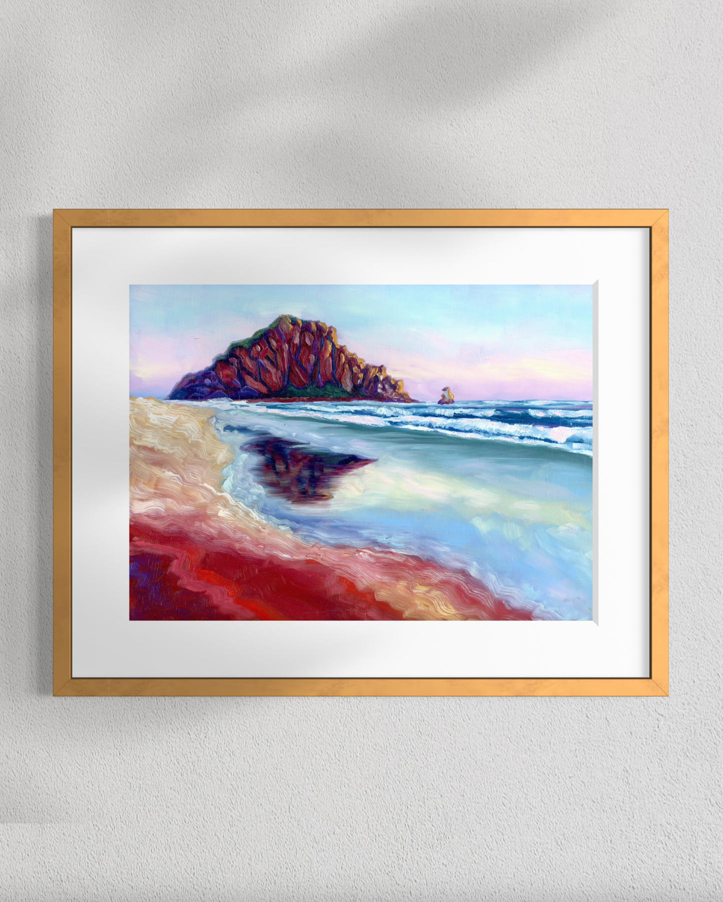 Framed artwork of a beach scene with a large rock formation on a white wall.