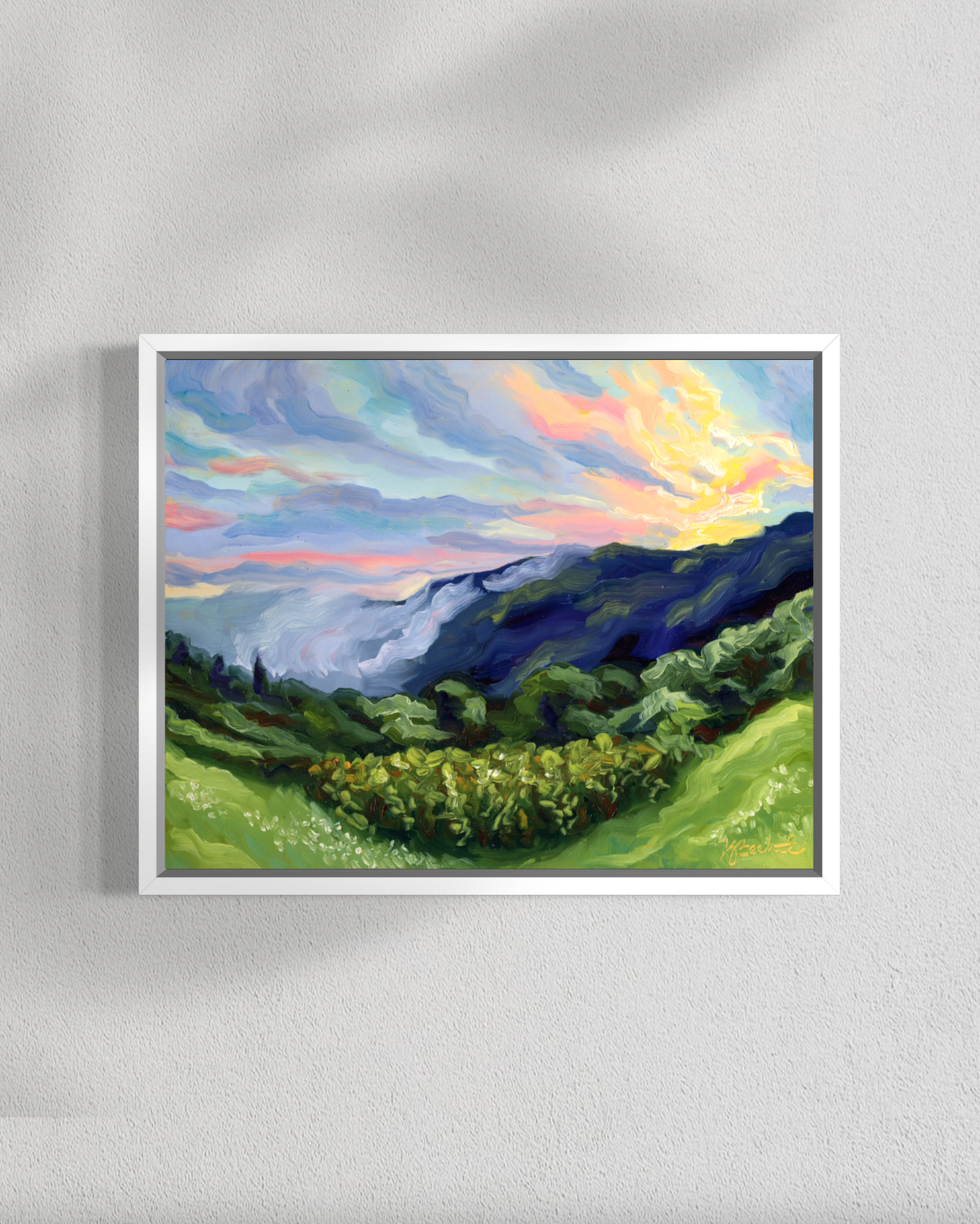 Framed painting of a landscape with mountains and colorful sky on a gray wall.