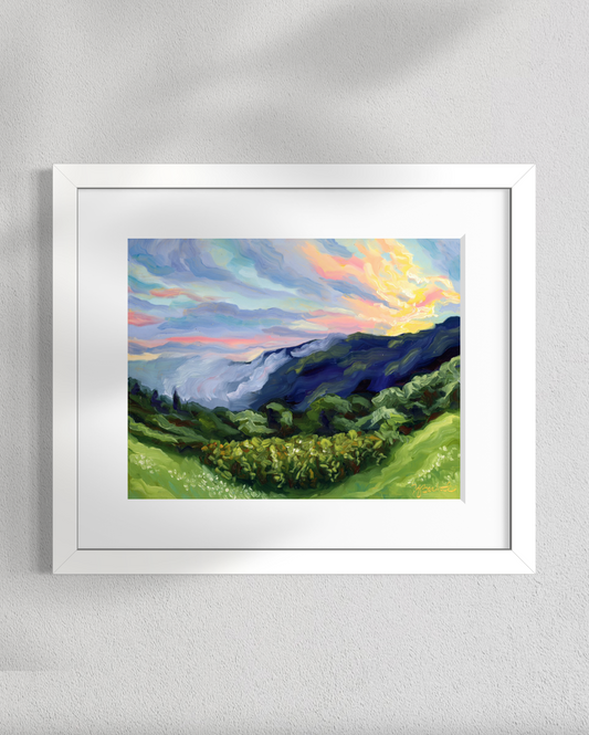 Framed painting of a landscape with mountains and a colorful sky on a white wall.