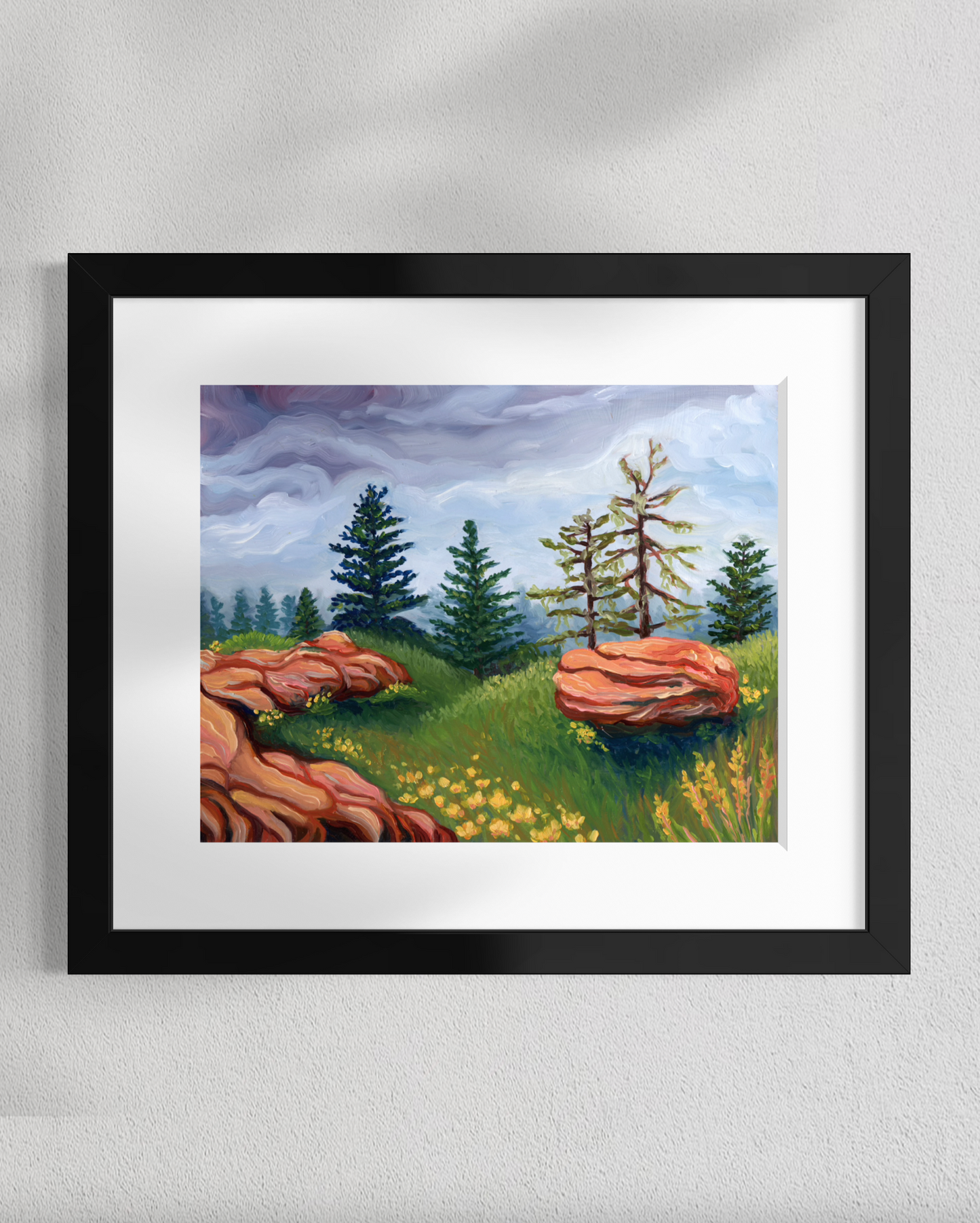 Framed painting of a landscape with trees, rocks, and flowers on a white wall.