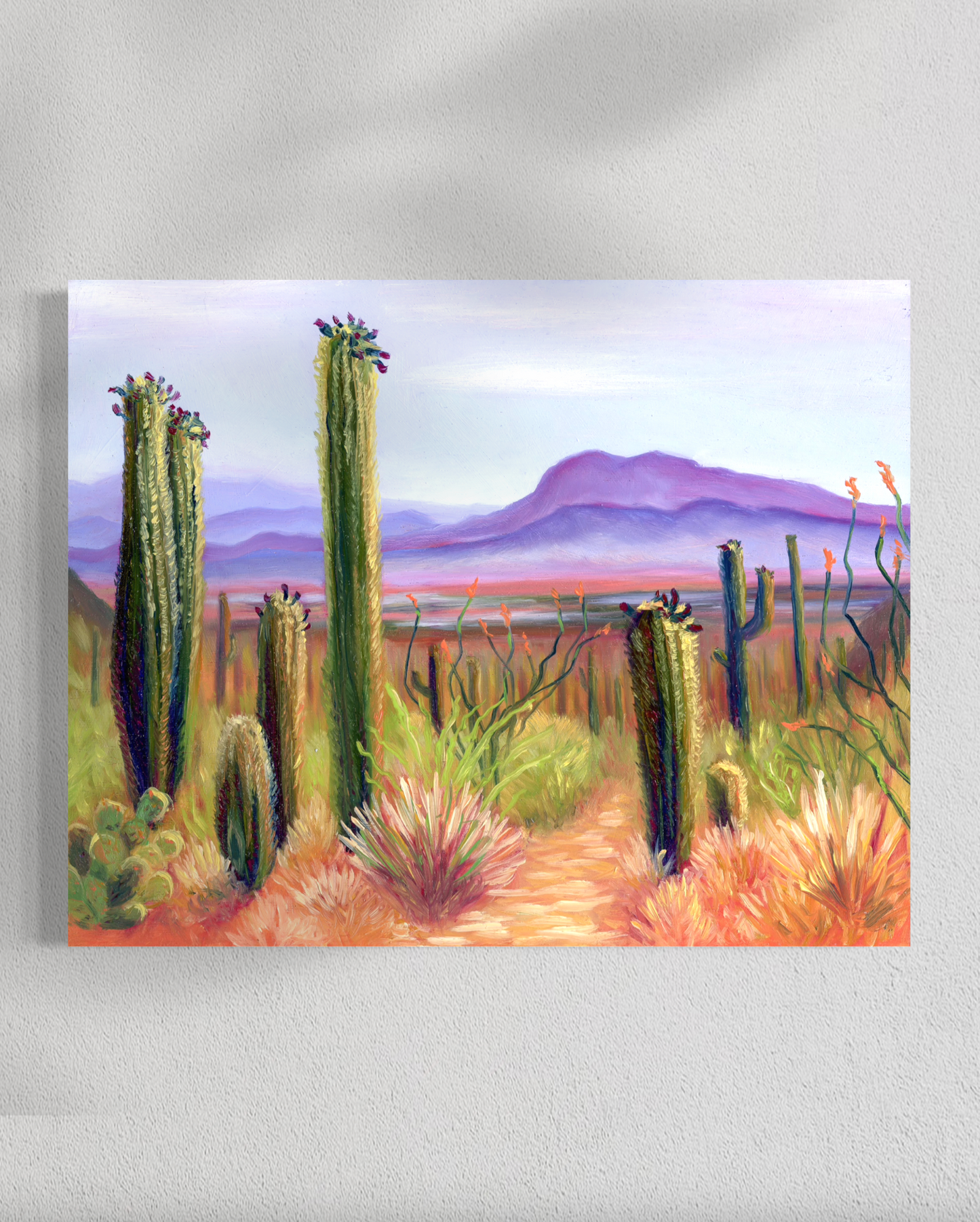 Painting of a desert landscape with cacti and mountains on a white wall.