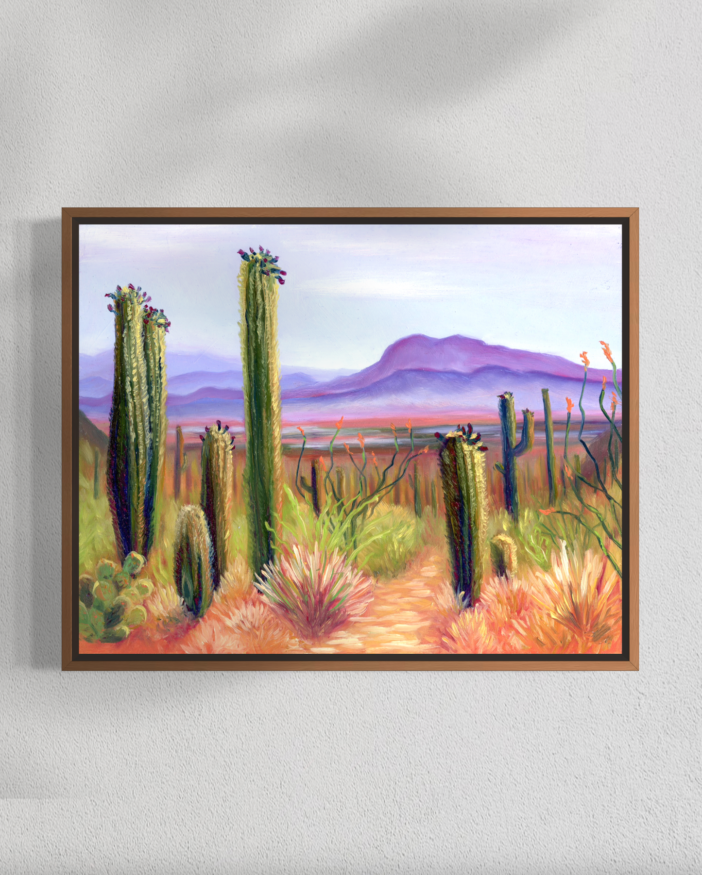 Framed artwork of a desert landscape with cacti on a white wall