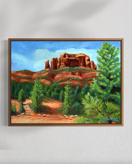 Framed painting of a desert landscape with rock formations and greenery on a white wall.