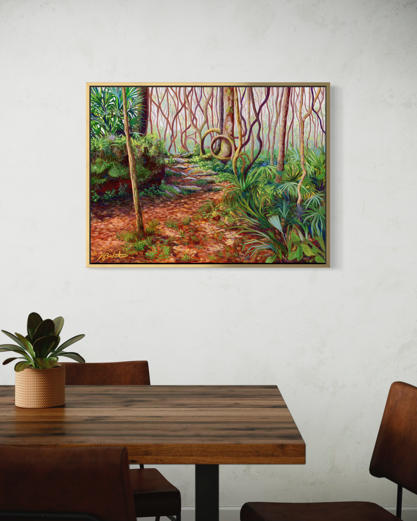 Framed painting of a forest scene on a wall above a wooden table.